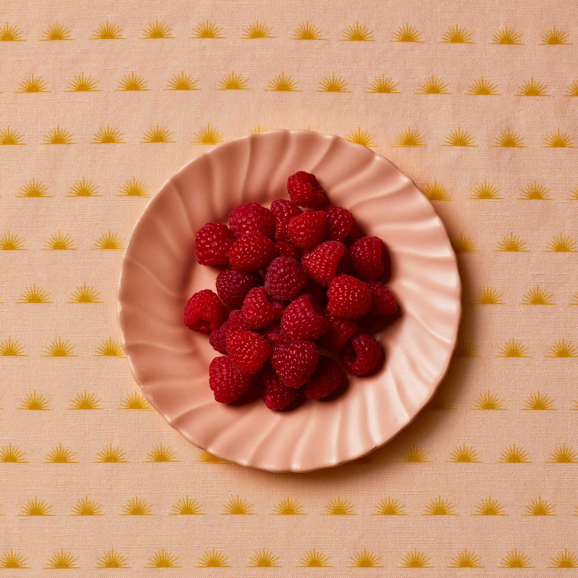 Raspberries sitting on a pink plate on top of a patterned tablecloth