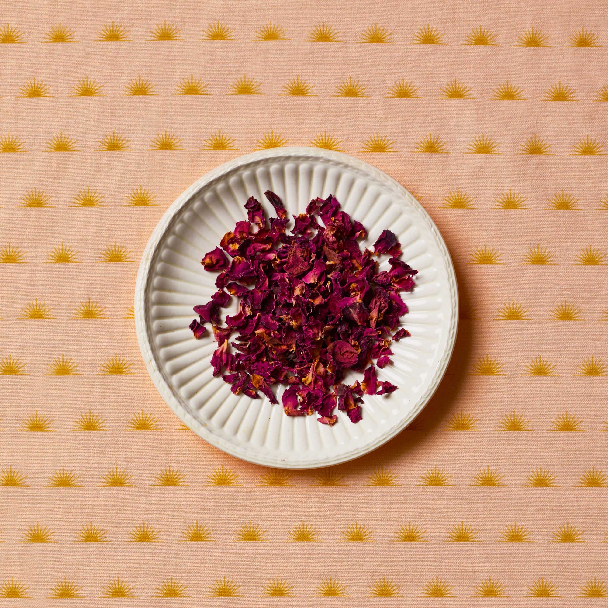 Rose petals sitting on a white plate on top of a patterned tablecloth