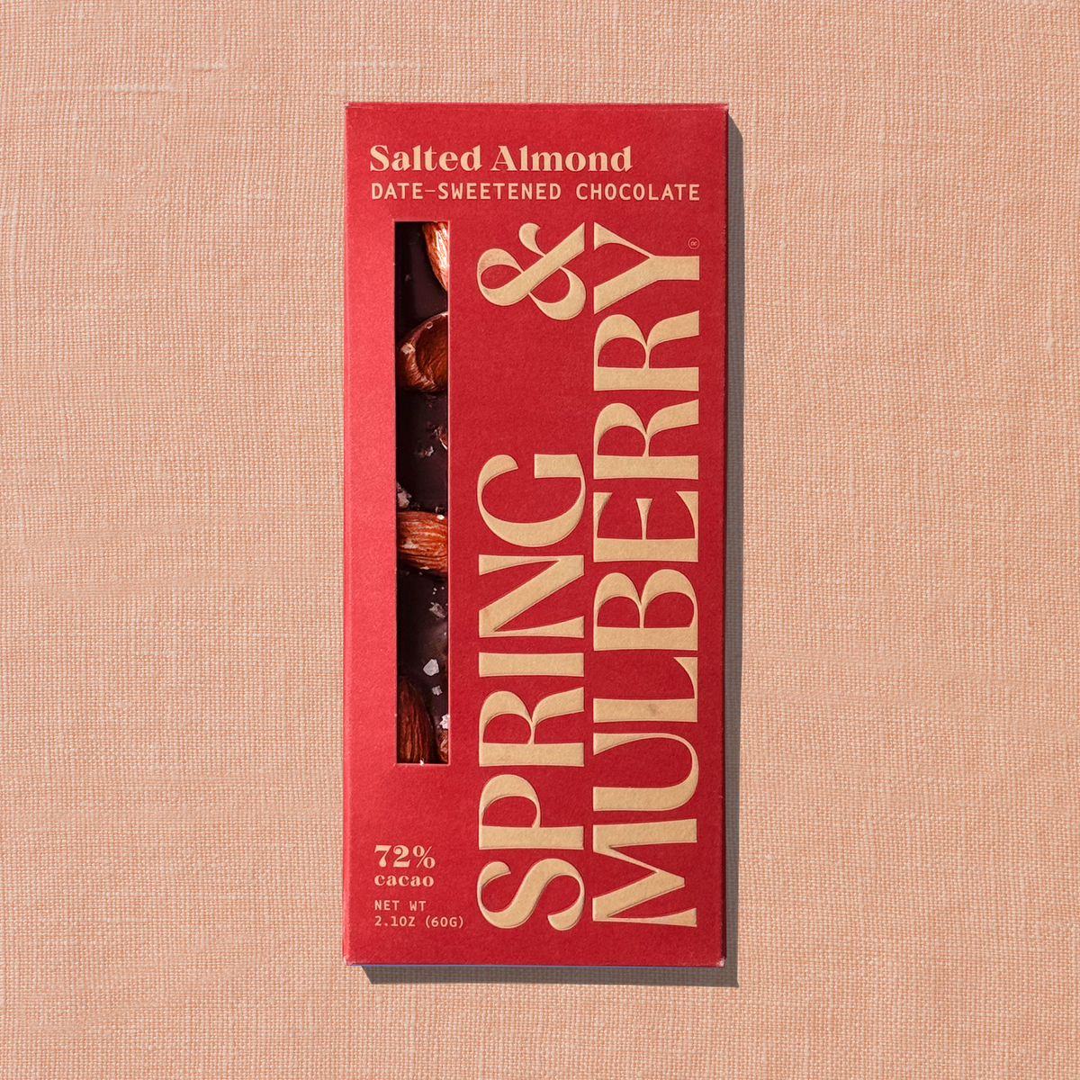 Front of Spring & Mulberry Salted Almond 72% cacao date-sweetened dark chocolate bar in red packaging with gold lettering, featuring a window showing whole almonds and flake salt, on a peach textured background.