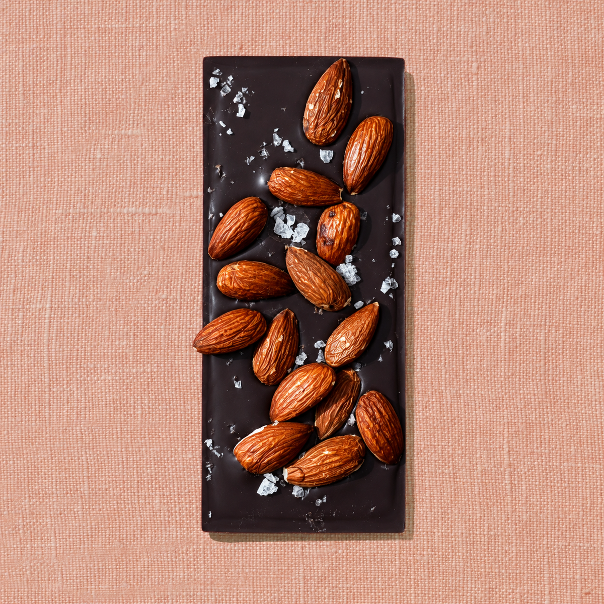 Spring & Mulberry Salted Almond dark chocolate bar topped with whole roasted almonds and flaky sea salt, photographed on a textured peach background.