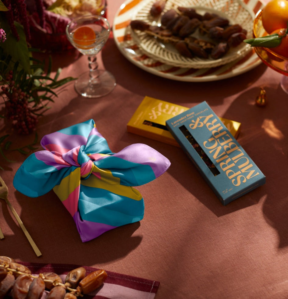 Fresh flowers, grapes, raspberries and almonds beside a citrus drink and a Spring & Mulberry chocolate box