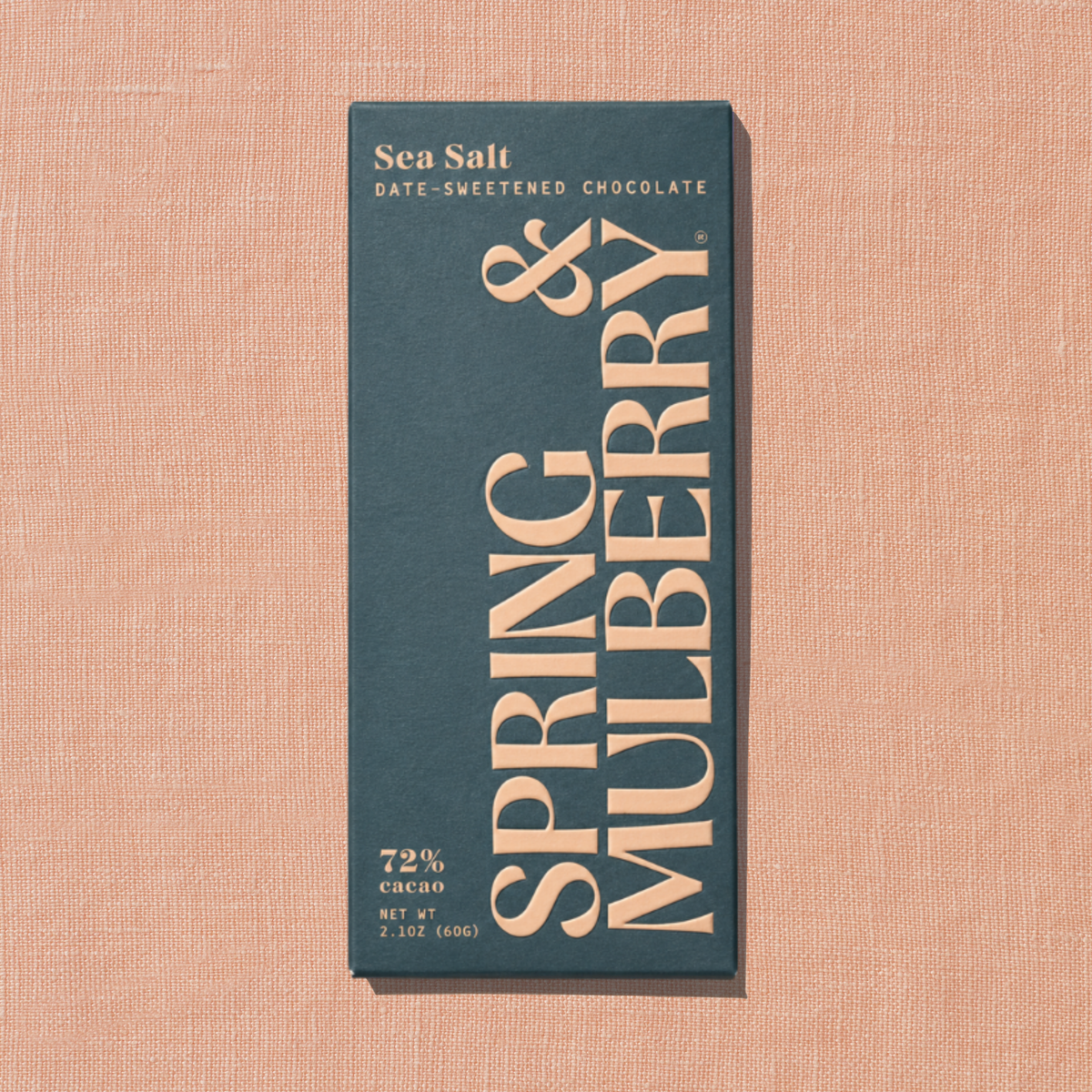 A grey Spring & Mulberry box labeled Sea Salt date-sweetened chocolate is laid on a light peach background. 