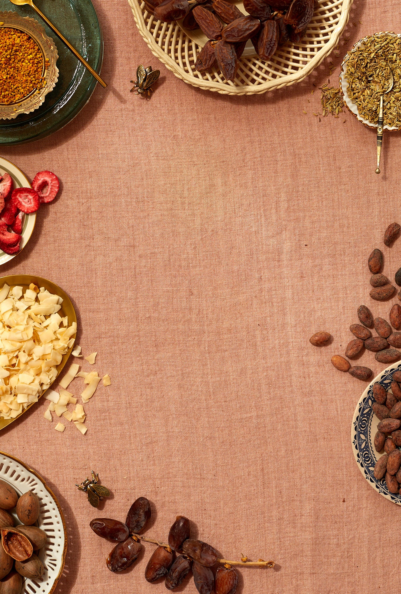 A peach colored linen tablecloth communicates the free shipping promotion. Around the edge of the image is a smattering of dates, nuts, cocnut, cacao beans, freeze dried strawberries, and pee pollen in mix-and-matched vintage bowls. 