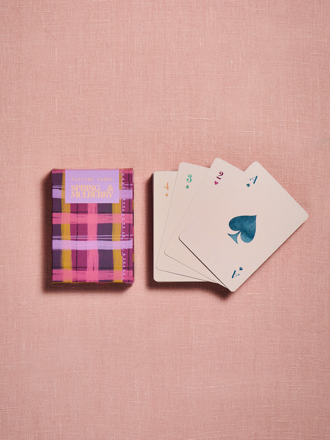Spring & Mulberry playing cards featuring a vibrant pink and purple plaid card box, displayed alongside a fan of colorful playing cards on a soft blush background.