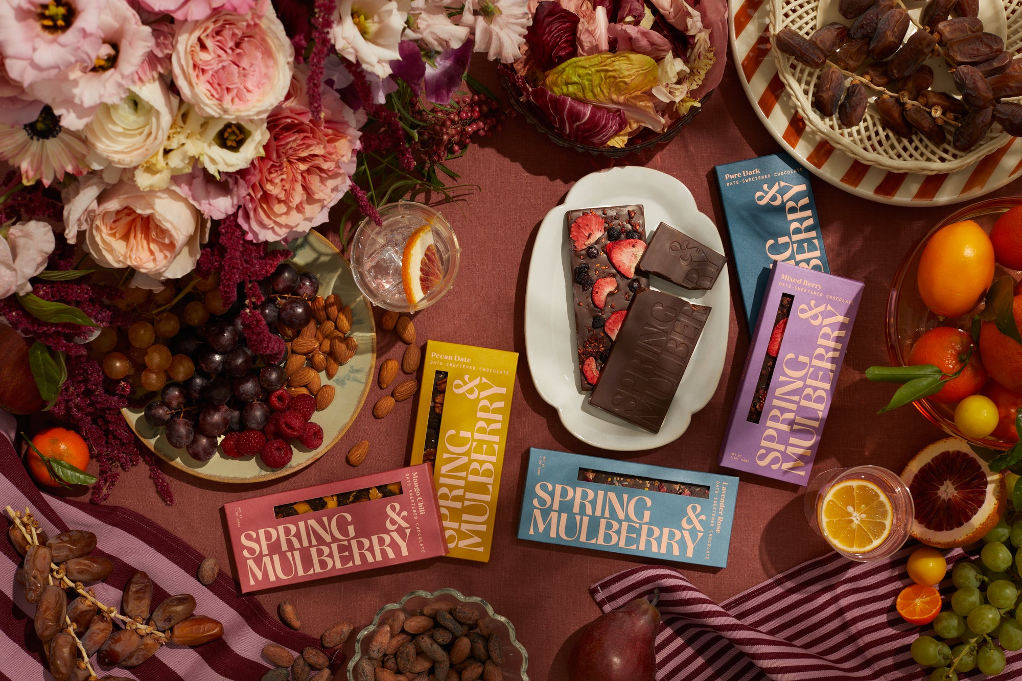 A tablescape filled with fruits and florals features Spring & Mulberry chocolate boxes anda a plate with two embellished chocolate bars.