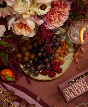 Tablescape filled with fruits, nuts and florals, with a Spring & Mulberry chocolate bar.