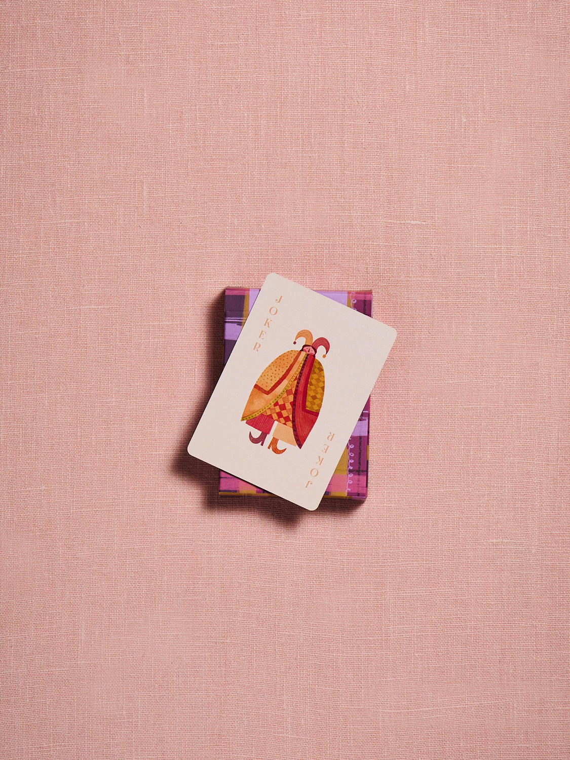 Spring & Mulberry playing card on top of a pink and purple plaid card box, displayed alongside a fan of colorful playing cards on a soft blush background.