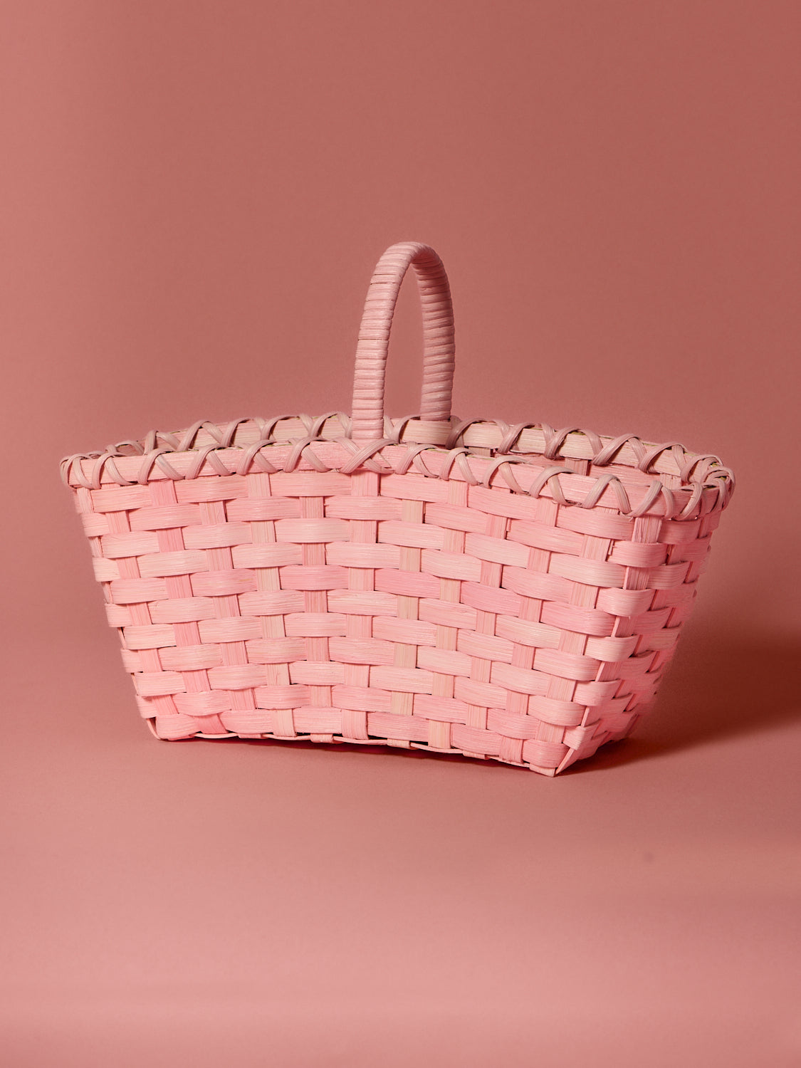 Handmade pink woven rattan handbag on a matching pink background. Designed for Spring & Mulberry by Underwater Weaving. 