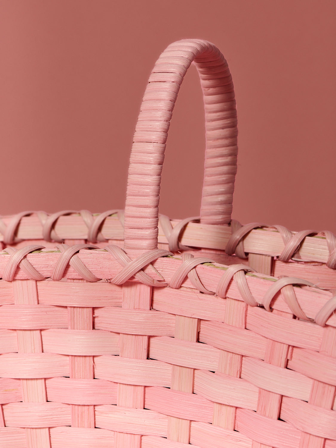 Closeup of handmade pink woven rattan handbag on a matching pink background. Designed for Spring & Mulberry by Underwater Weaving. 