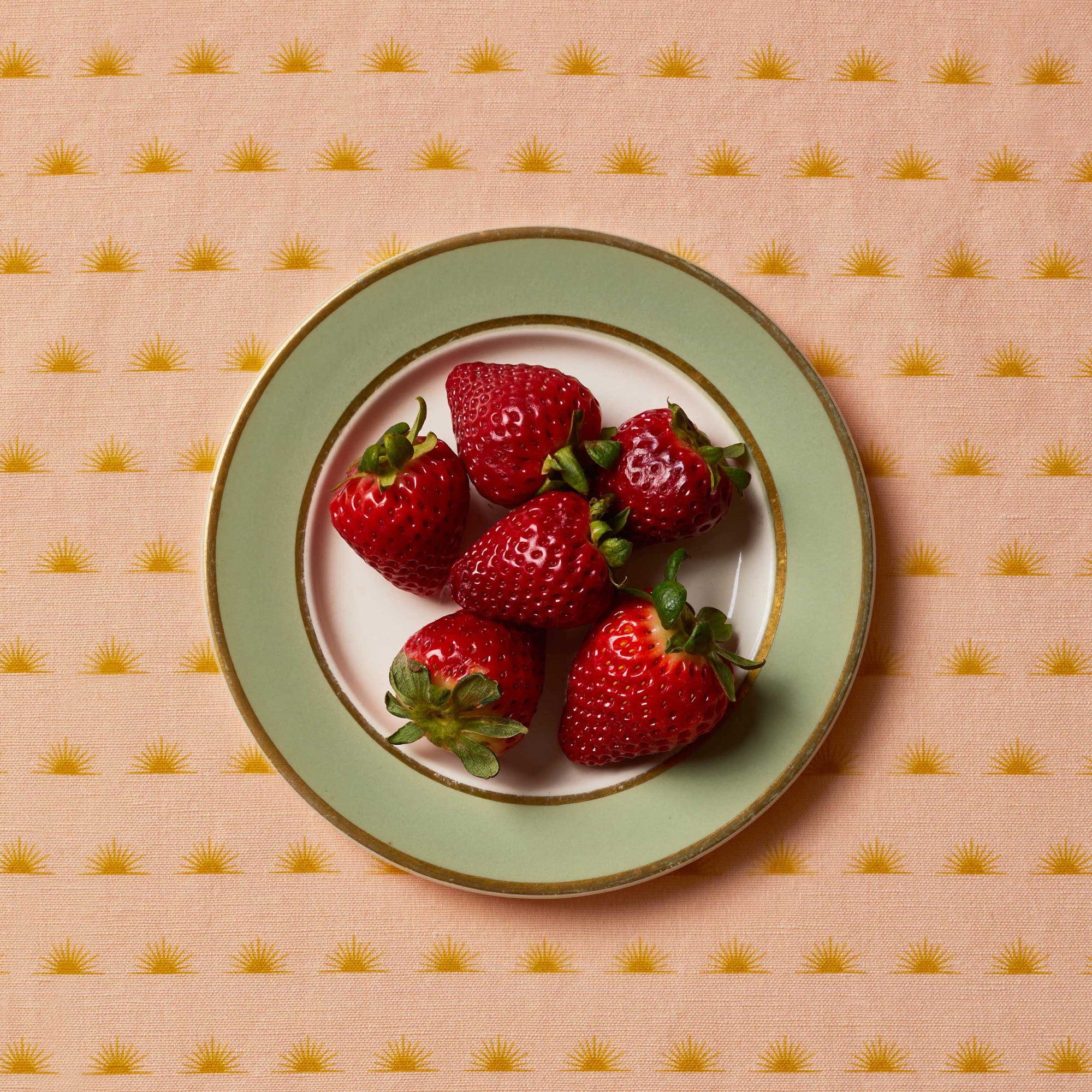 Strawberries sitting on a white and green plate on top of a patterned tablecloth