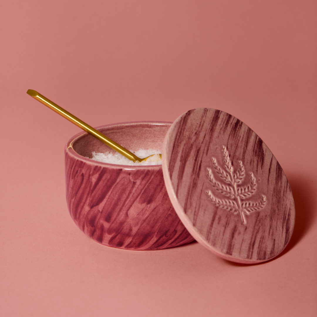 Handpainted ceramic salt cellar with lid and gold spoon on a pink background