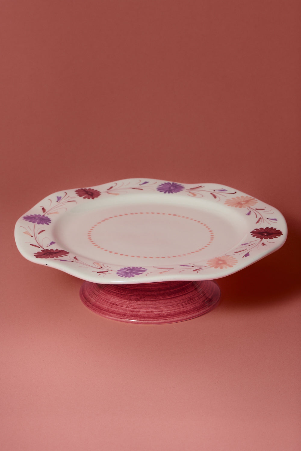 Vaisselle hand painted cake stand with mulberry, peach and lavender floral design on a pink background