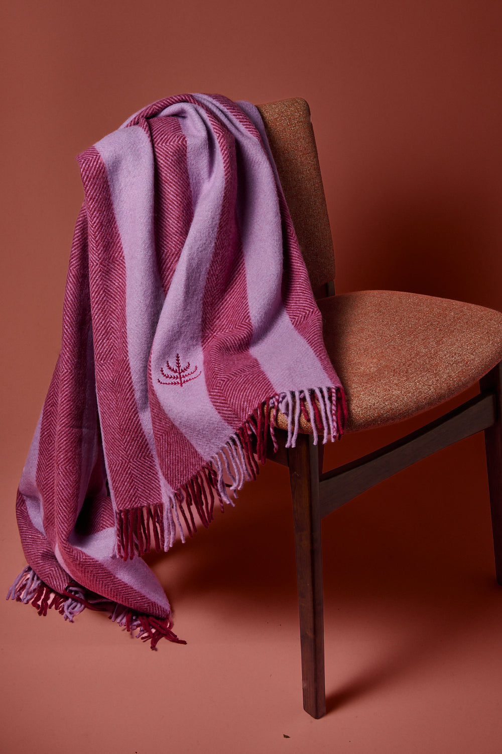 Lilac and mulberry striped blanket with the spring and Mulberry logo draped over a wooden chair against a brown background